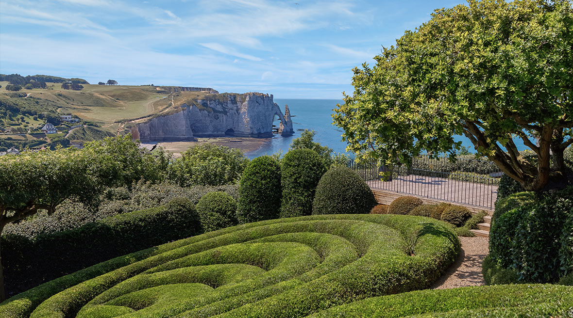 View of the famous white chalk Etretat cliffs from the garden (Jardin d'Etretat) with visible ocean stretch and swirling green hedge in the garden